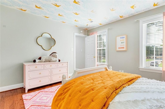 bedroom with wood finished floors, baseboards, and multiple windows