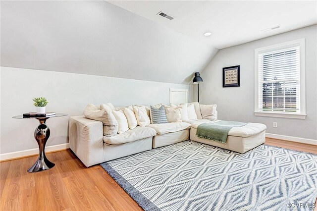 living room featuring vaulted ceiling, light wood-type flooring, visible vents, and baseboards