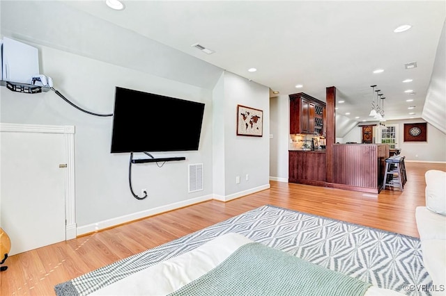 living area featuring lofted ceiling, light wood-style flooring, and visible vents