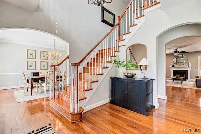 staircase with a high ceiling, wood finished floors, ceiling fan with notable chandelier, and arched walkways