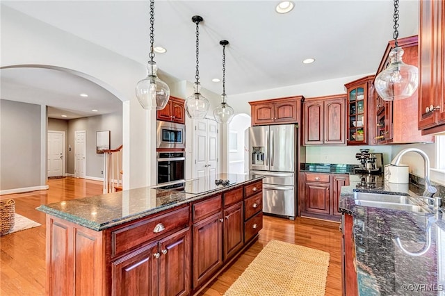 kitchen with arched walkways, light wood-style floors, appliances with stainless steel finishes, and a sink