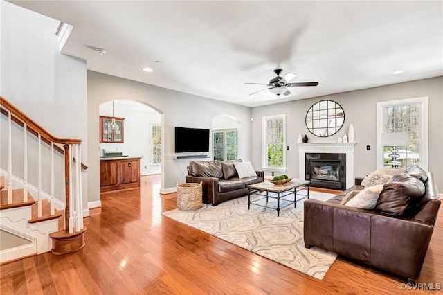 living room with a wealth of natural light, wood finished floors, arched walkways, and a high end fireplace