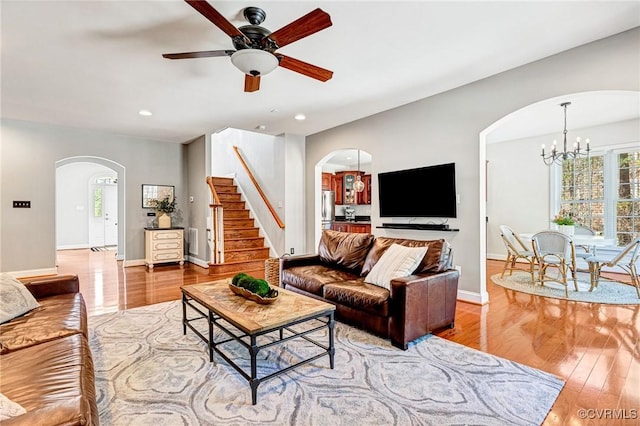 living area with arched walkways, stairs, ceiling fan with notable chandelier, and wood finished floors