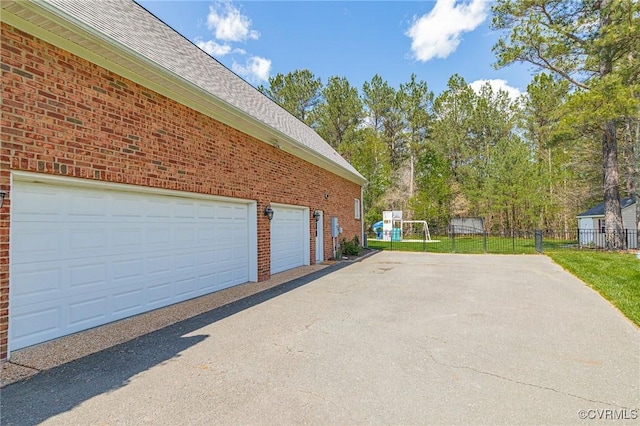 view of home's exterior featuring brick siding, fence, aphalt driveway, a garage, and roof with shingles