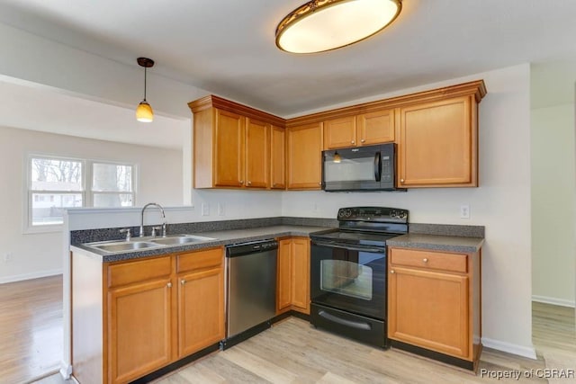 kitchen with a sink, black appliances, light wood-style floors, dark countertops, and decorative light fixtures
