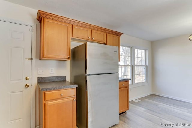 kitchen featuring dark countertops, baseboards, light wood-type flooring, freestanding refrigerator, and brown cabinetry