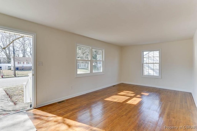 spare room featuring wood finished floors, visible vents, and baseboards