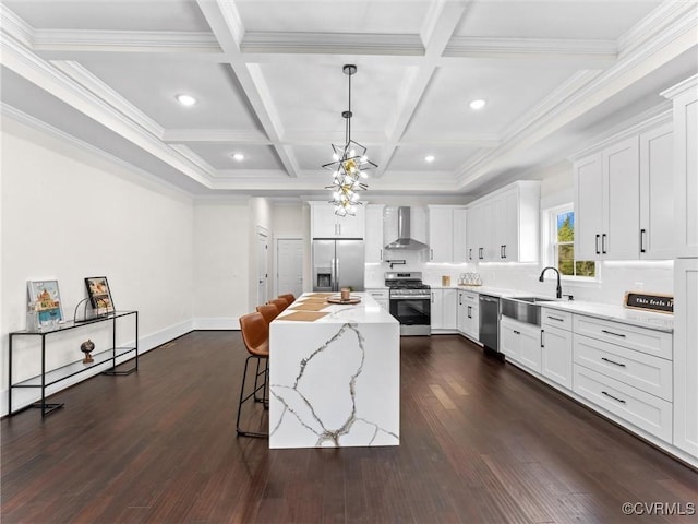 kitchen with wall chimney range hood, appliances with stainless steel finishes, a sink, a breakfast bar area, and dark wood-style floors