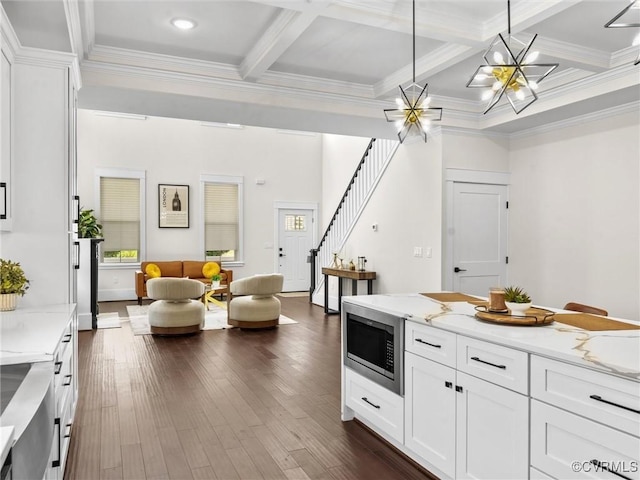 kitchen with hanging light fixtures, white cabinets, dark wood-style flooring, beam ceiling, and stainless steel microwave