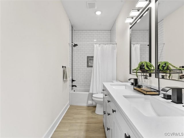 bathroom featuring toilet, wood finished floors, double vanity, and a sink