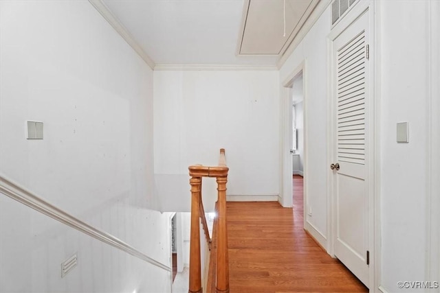 corridor featuring attic access, ornamental molding, and light wood-style flooring