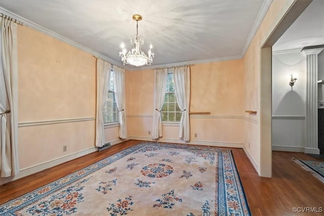 interior space with wood finished floors, ornate columns, ornamental molding, and an inviting chandelier