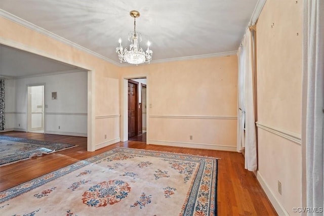 empty room with a chandelier, wood finished floors, baseboards, and ornamental molding