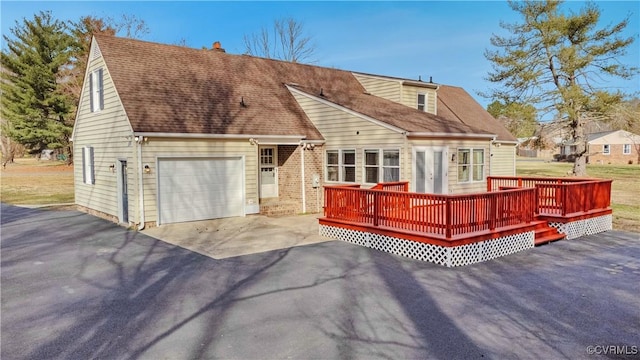 view of front of home with a deck, an attached garage, driveway, and roof with shingles