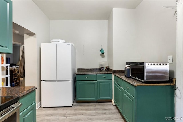 kitchen with green cabinets, light wood finished floors, dark countertops, and freestanding refrigerator