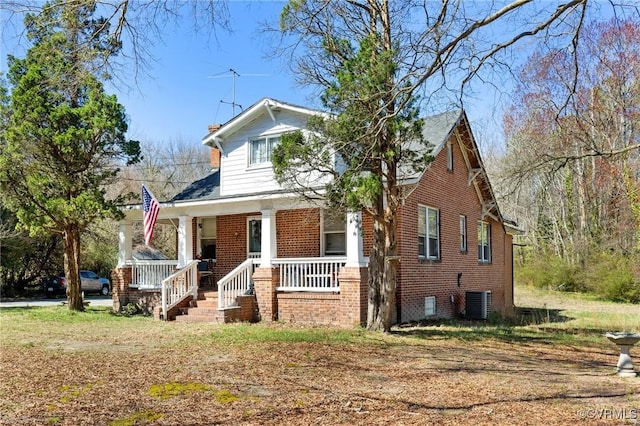 bungalow featuring covered porch, brick siding, and central air condition unit