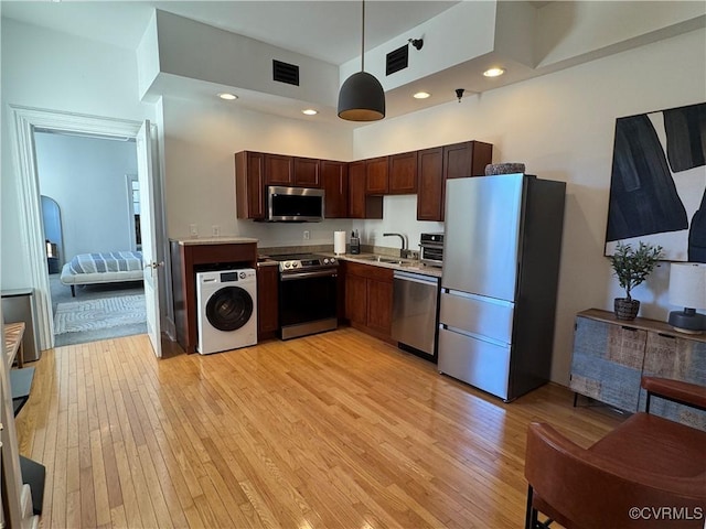 kitchen with visible vents, washer / dryer, light wood-style flooring, stainless steel appliances, and a sink