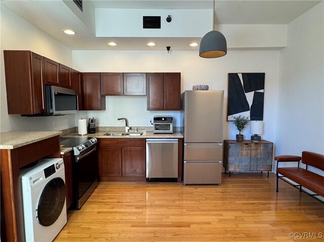 kitchen with visible vents, a sink, appliances with stainless steel finishes, light wood finished floors, and washer / dryer