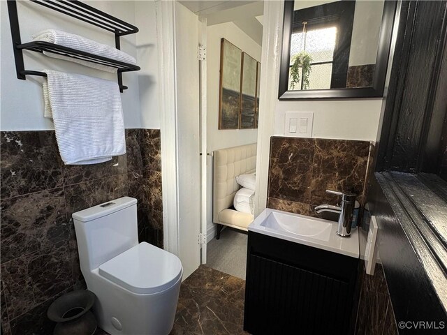 half bath featuring marble finish floor, toilet, tile walls, and vanity