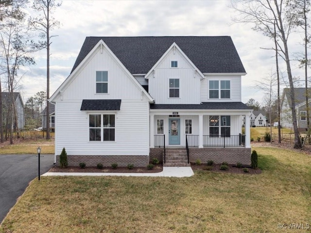 modern farmhouse featuring covered porch, board and batten siding, a front yard, and a shingled roof