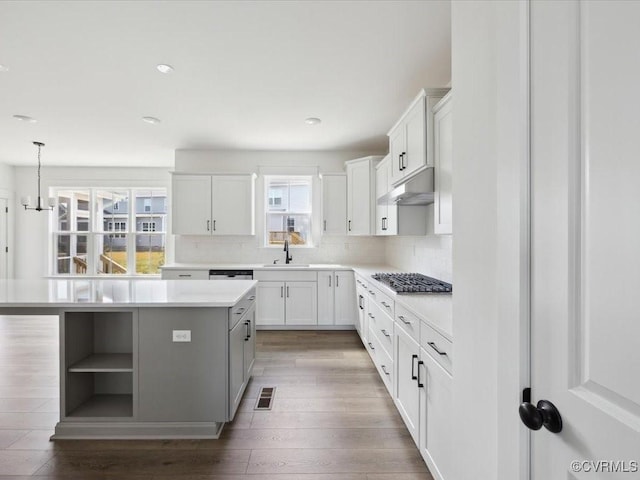 kitchen featuring light countertops, visible vents, a kitchen island, under cabinet range hood, and open shelves