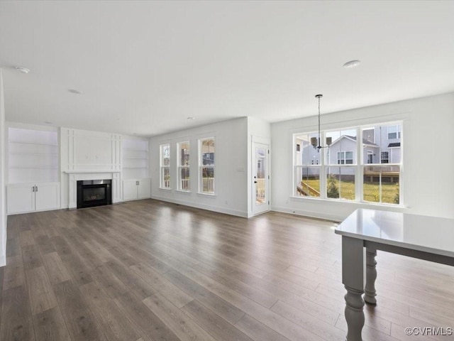 unfurnished living room featuring dark wood-type flooring, baseboards, a glass covered fireplace, and a notable chandelier