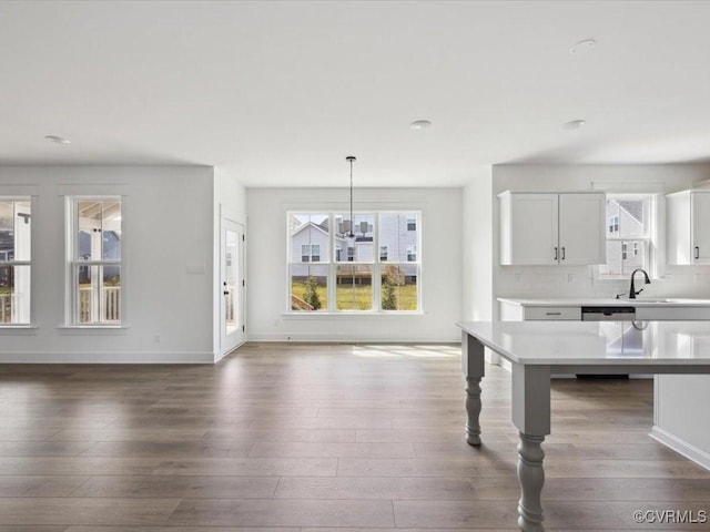 kitchen with light countertops, a sink, wood finished floors, dishwasher, and decorative backsplash