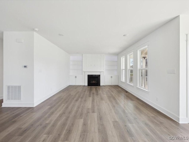 unfurnished living room with light wood-type flooring, baseboards, a fireplace, and visible vents