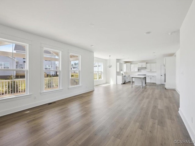 unfurnished living room with baseboards, visible vents, and wood finished floors