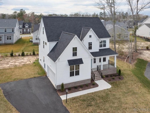 modern inspired farmhouse featuring a front yard, a shingled roof, covered porch, and aphalt driveway