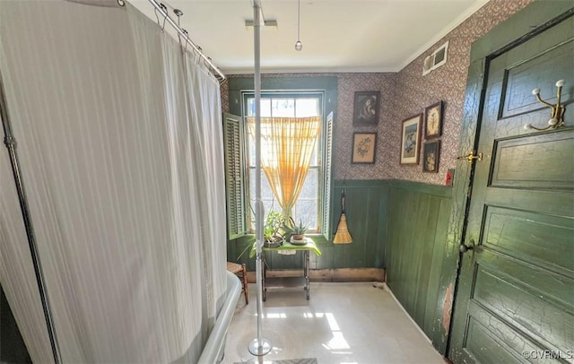 interior space with a wainscoted wall, wallpapered walls, visible vents, and ornamental molding