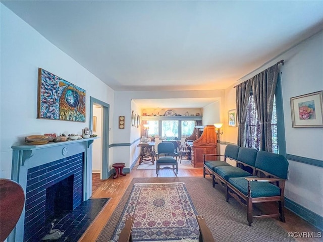 living area featuring a tiled fireplace, baseboards, and wood finished floors