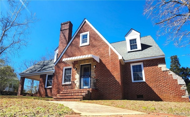 view of front of home featuring a chimney, a front lawn, brick siding, and roof with shingles