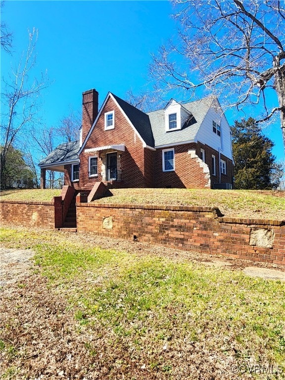 view of front of property featuring a chimney, brick siding, and a front yard