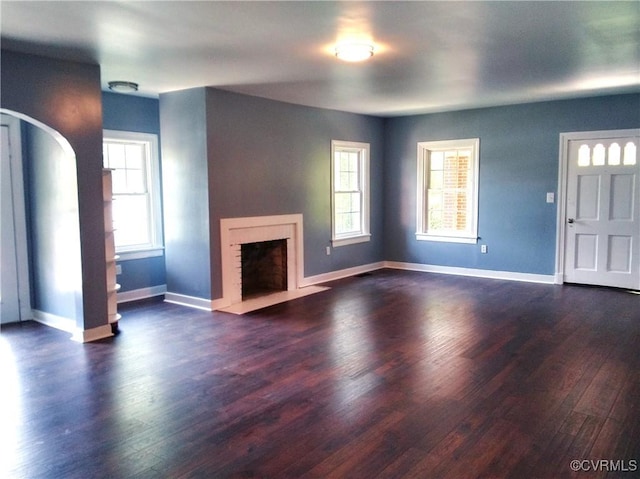 unfurnished living room with a fireplace with flush hearth, a wealth of natural light, arched walkways, and dark wood-type flooring