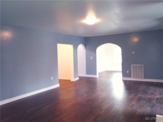 spare room with baseboards, wood finished floors, visible vents, and arched walkways