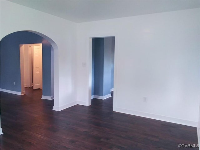 spare room featuring arched walkways, baseboards, and dark wood-style floors