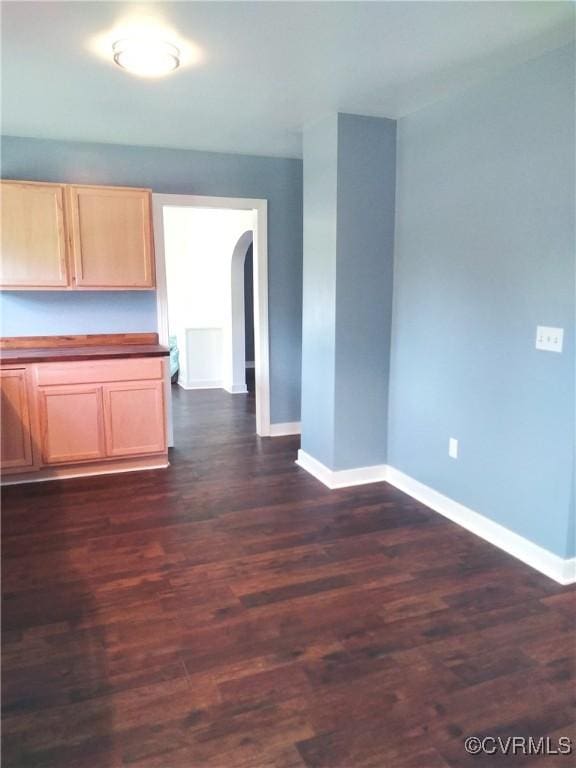 interior space featuring arched walkways, light brown cabinets, baseboards, and dark wood-style flooring
