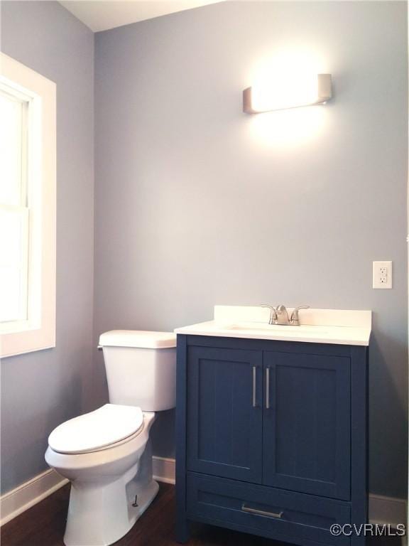 half bathroom featuring wood finished floors, vanity, toilet, and baseboards