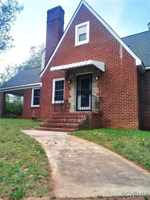view of front of house with a chimney, brick siding, a front yard, and roof with shingles