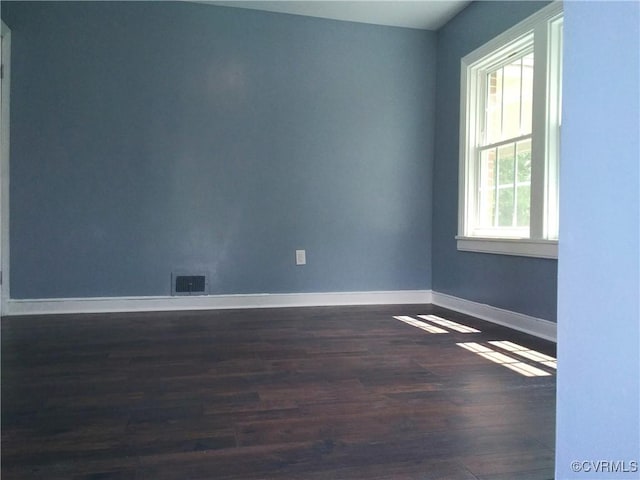 spare room with dark wood-type flooring, visible vents, and baseboards