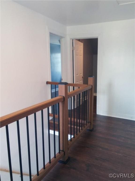corridor featuring baseboards, wood finished floors, and an upstairs landing
