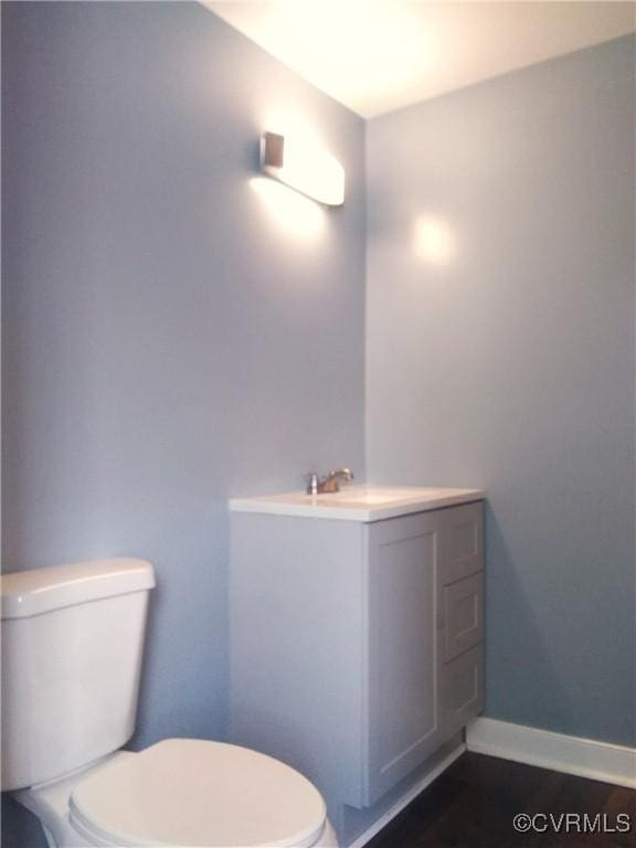 half bath featuring baseboards, vanity, and toilet