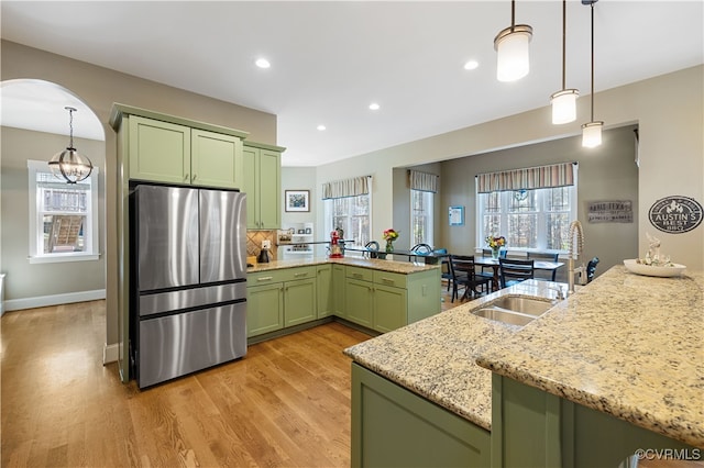 kitchen featuring light wood finished floors, a sink, green cabinets, a peninsula, and freestanding refrigerator