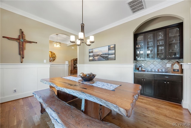 dining space with arched walkways, a wainscoted wall, light wood-type flooring, visible vents, and crown molding