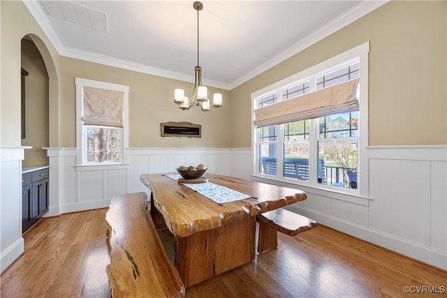 dining space with crown molding, visible vents, a chandelier, a wainscoted wall, and light wood finished floors