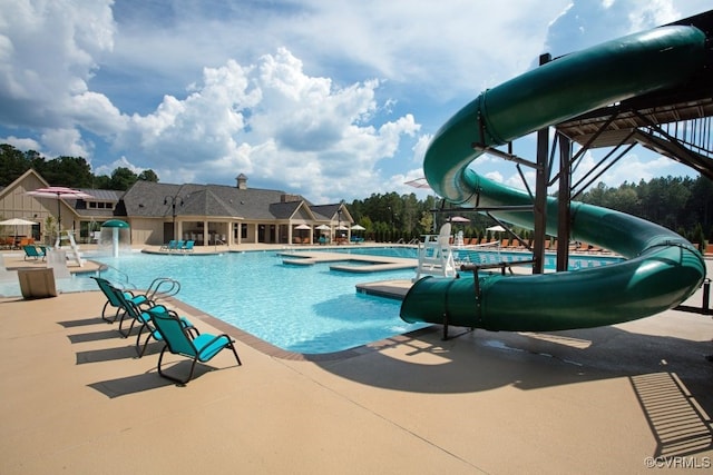 community pool featuring a patio, a water slide, and a hot tub