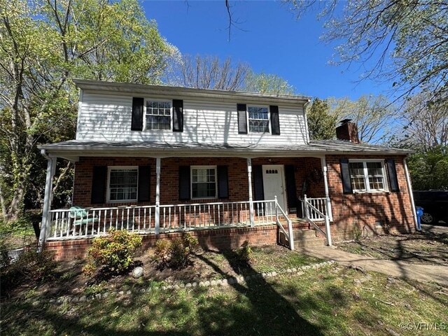 traditional-style house featuring a chimney, covered porch, and brick siding