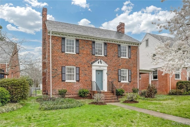 view of front of home featuring a chimney, fence, brick siding, and a front yard