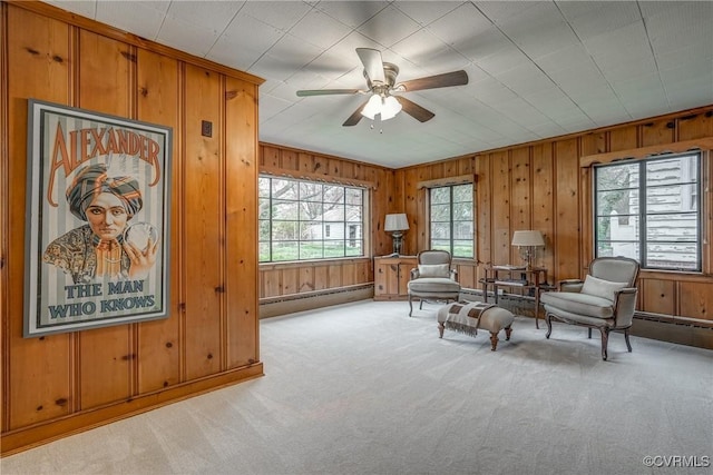 living area featuring a baseboard radiator, a ceiling fan, light carpet, and wooden walls